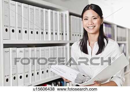 Businesswoman holding folder in library View Large Photo Image Stock Photo - Businesswoman holding folder in library. Fotosearch