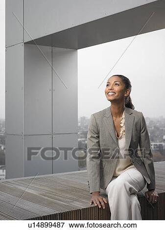 Stock Photo - Businesswoman sitting on building ledge. Fotosearch