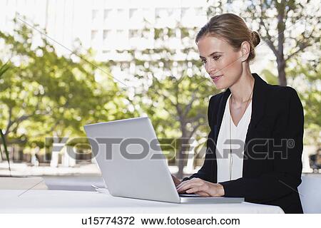 Stock Image - Businesswoman using laptop outdoors. Fotosearch