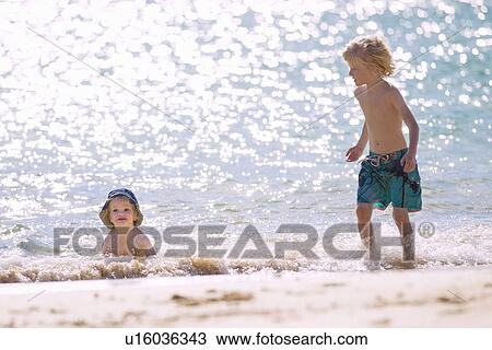 Stock Image - Children playing in waves on beach. Fotosearch
