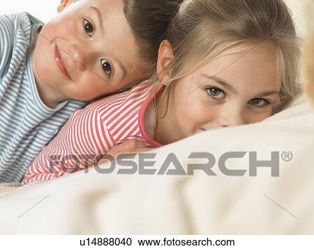 Stock Image - Children smiling together on bed. Fotosearch