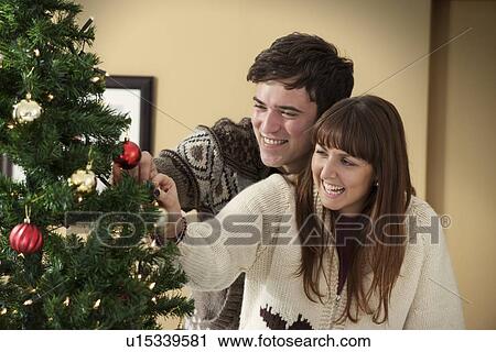 Stock Image - Couple decorating Christmas tree. Fotosearch
