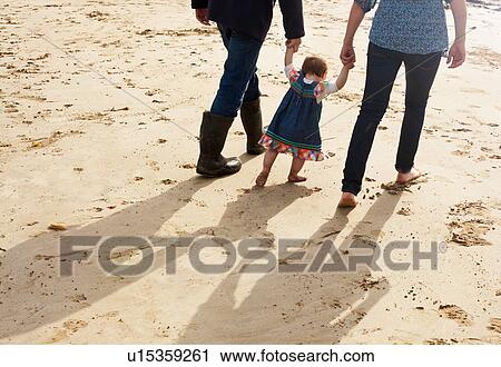 Couple helping toddler girl walk on beach View Large Photo Image Stock Image - Couple helping toddler girl walk on beach. Fotosearch