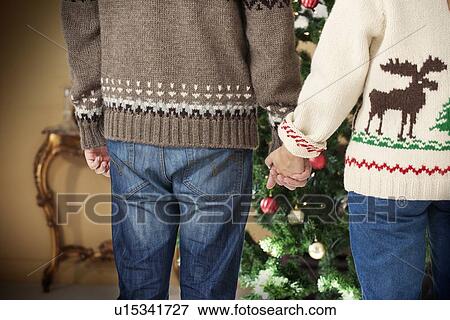 Couple holding hands by Christmas tree View Large Photo Image Stock Photo - Couple holding hands by Christmas tree. Fotosearch