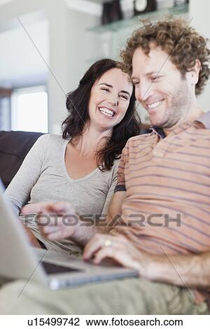 Stock Image - Couple using laptop together on sofa. Fotosearch