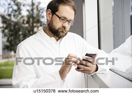 Doctor using cell phone at window View Large Photo Image Stock Photo - Doctor using cell phone at window. Fotosearch