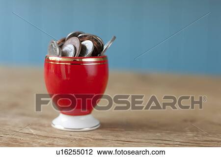 Stock Image - Egg cup full of money on desk. Fotosearch
