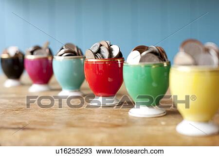 Stock Image - Egg cups full of money on desk. Fotosearch