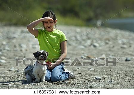 Stock Image - Girl sitting with dog in field. Fotosearch