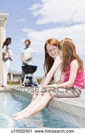 Stock Image - Girls dangling feet in swimming pool. Fotosearch