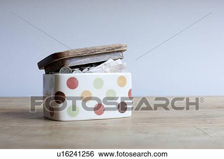 Stock Photograph - Jar full of money on desk. Fotosearch