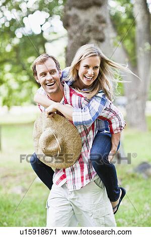 Stock Image - Man carrying girlfriend in park. Fotosearch