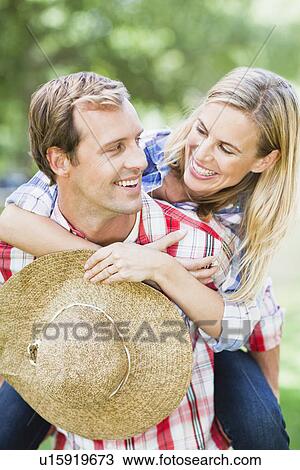 Stock Image - Man carrying girlfriend in park. Fotosearch