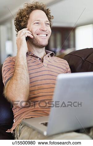 Stock Image - Man on laptop talking on cell phone. Fotosearch