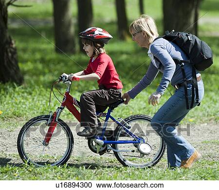 Mother pushing son on bicycle in park View Large Photo Image Stock Image - Mother pushing son on bicycle in park. Fotosearch