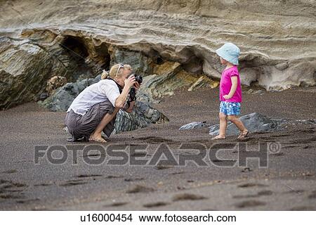 Picture - Mother taking picture of daughter on beach. Fotosearch