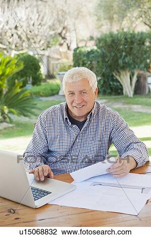 Stock Image - Older man paying bills on laptop. Fotosearch