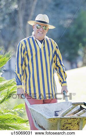 Stock Image - Older man pushing wheelbarrow outdoors. Fotosearch