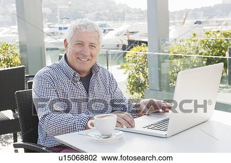 Stock Image - Older man using laptop in cafe. Fotosearch