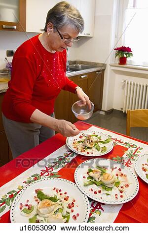 Stock Image - Older woman plating dinner in kitchen. Fotosearch