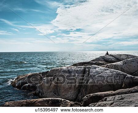 Person sitting on coastal rock formation View Large Photo Image Stock Photo - Person sitting on coastal rock formation. Fotosearch
