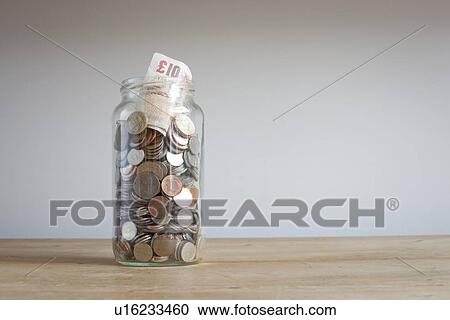 Stock Image - Savings jar on desk. Fotosearch