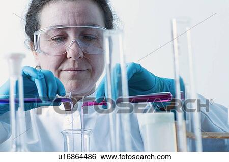 Stock Photograph - Scientist pouring liquid into beaker. Fotosearch