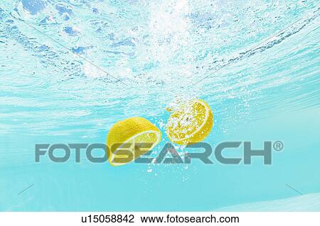Stock Image - Sliced lemon splashing into water. Fotosearch