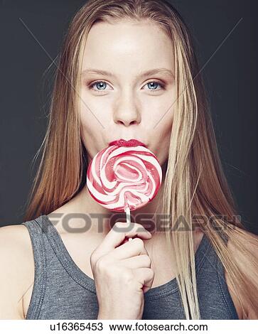 Stock Image - Smiling woman eating lollipop. Fotosearch