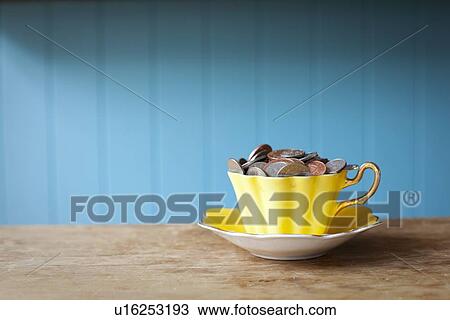 Stock Image - Teacup full of money on desk. Fotosearch