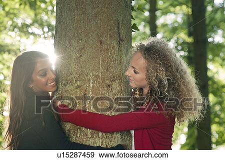 Teenage girls hugging tree in forest View Large Photo Image Stock Photo - Teenage girls hugging tree in forest. Fotosearch