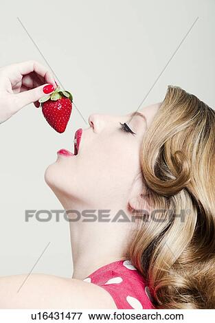 Stock Photo - Woman eating strawberry indoors. Fotosearch