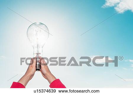 Stock Photo - Woman holding light bulb in sky. Fotosearch