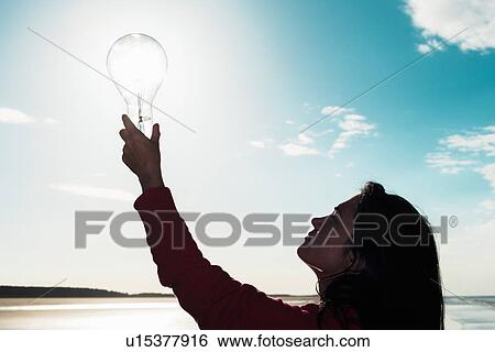 Woman holding light bulb in sky View Large Photo Image Stock Photograph - Woman holding light bulb in sky. Fotosearch