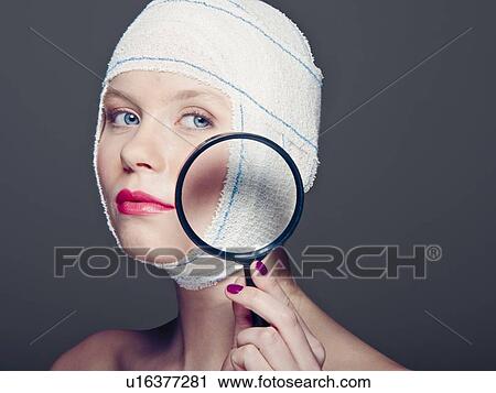 Stock Image - Woman in bandages with magnifying glass. Fotosearch