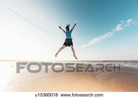 Stock Photo - Woman jumping with light bulb on beach. Fotosearch