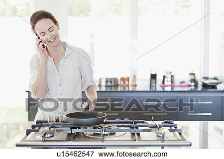 Stock Photo - Woman on cell phone cooking. Fotosearch