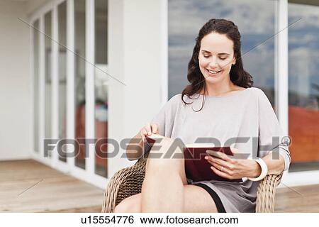Stock Photograph - Woman reading book in backyard. Fotosearch
