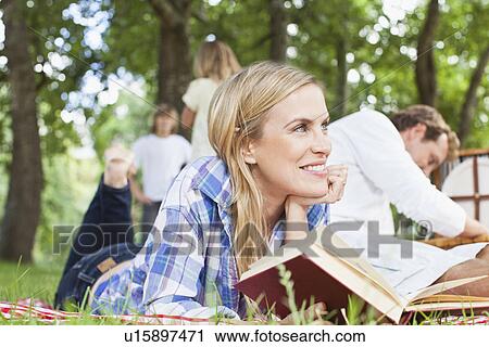 Stock Image - Woman reading on blanket in park. Fotosearch