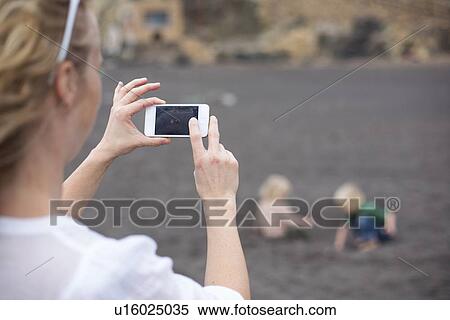 Stock Photography - Woman taking cell phone picture on beach. Fotosearch