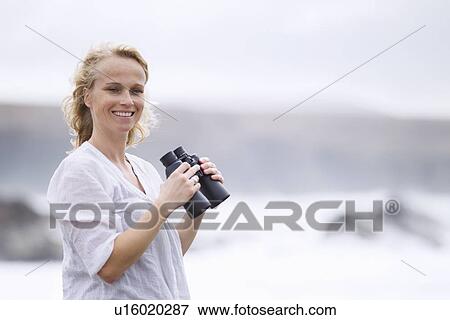 Stock Photo - Woman using binoculars on beach. Fotosearch