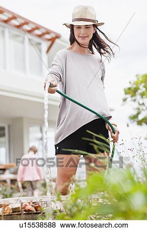 Woman watering plants in backyard View Large Photo Image Stock Photo - Woman watering plants in backyard. Fotosearch