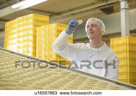 Stock Image - Worker examining biscuit in factory. Fotosearch