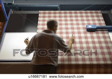 Stock Image - Worker examining fabric in textile mill. Fotosearch