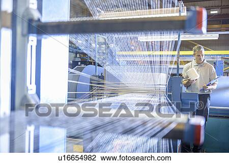 Worker examining loom in textile mill View Large Photo Image Stock Image - Worker examining loom in textile mill. Fotosearch