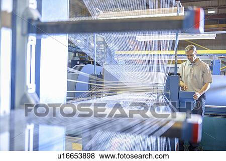 Stock Photo - Worker examining loom in textile mill. Fotosearch