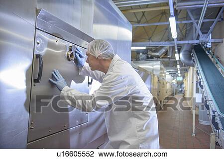 Stock Image - Worker examining oven in biscuit factory. Fotosearch