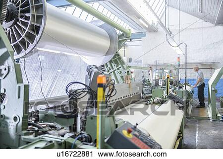 Stock Image - Worker using loom in textile mill. Fotosearch