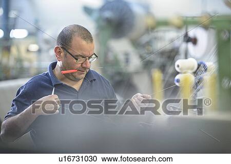 Stock Image - Worker using loom in textile mill. Fotosearch