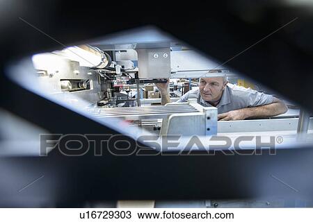Stock Image - Worker using machinery in textile mill. Fotosearch